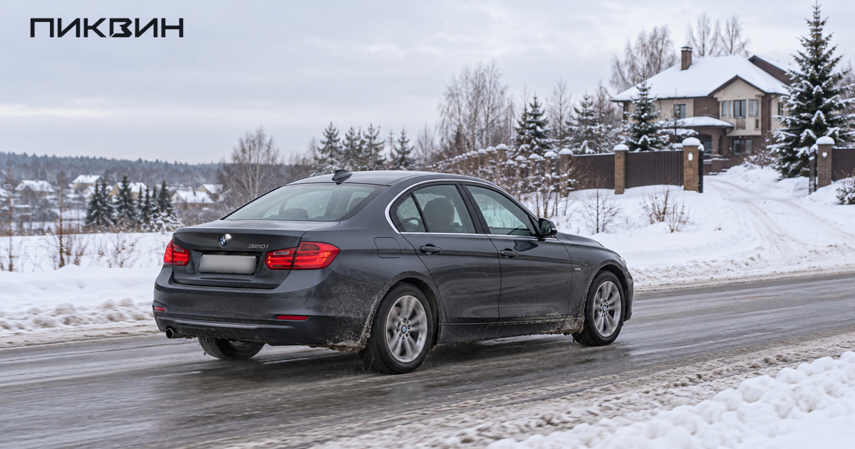 Заднеприводный седан BMW 320i на очищенной зимней дороге возле подъезда к дому.
