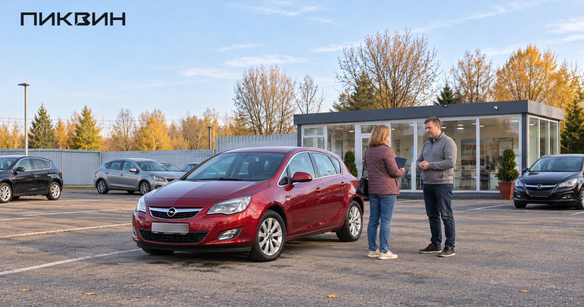 Покупательница с папкой разговаривает с продавцом рядом с красным Opel Astra на площадке подержанных автомобилей.