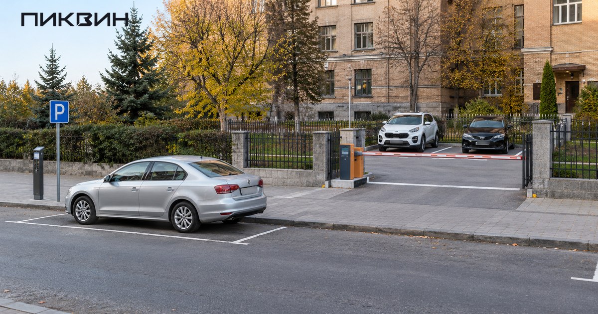 Автомобиль в уличном парковочном месте рядом с отдельной огороженной стоянкой со шлагбаумом.