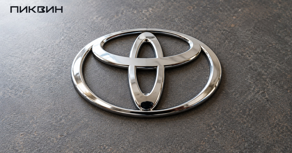 Хромированная овальная эмблема Toyota на нейтральной поверхности, видны три пересекающихся эллипса.