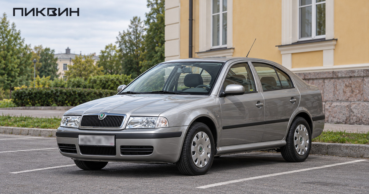 Серебристая Skoda Octavia первого поколения стоит на свободной площадке у невысокого городского здания.