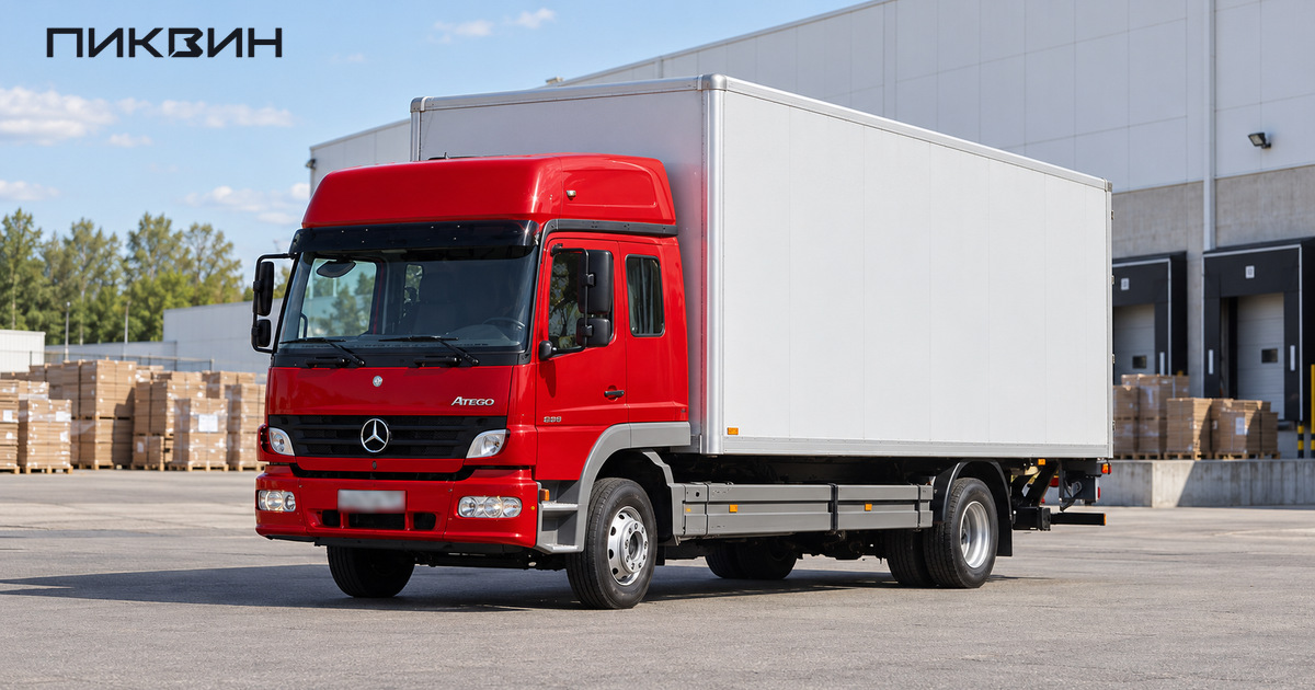 Красный Mercedes-Benz Atego с белым промтоварным фургоном стоит на свободной площадке у склада упаковочных материалов.