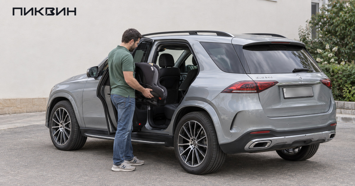 Мужчина держит детское кресло у открытой задней двери серебристого Mercedes-Benz GLE.