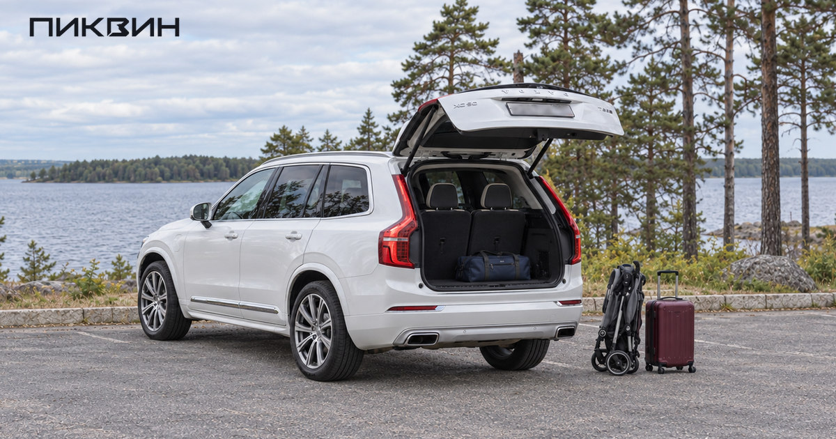 Белый Volvo XC90 с открытой крышкой багажника и поднятым третьим рядом; рядом стоят сложенная коляска и чемодан.