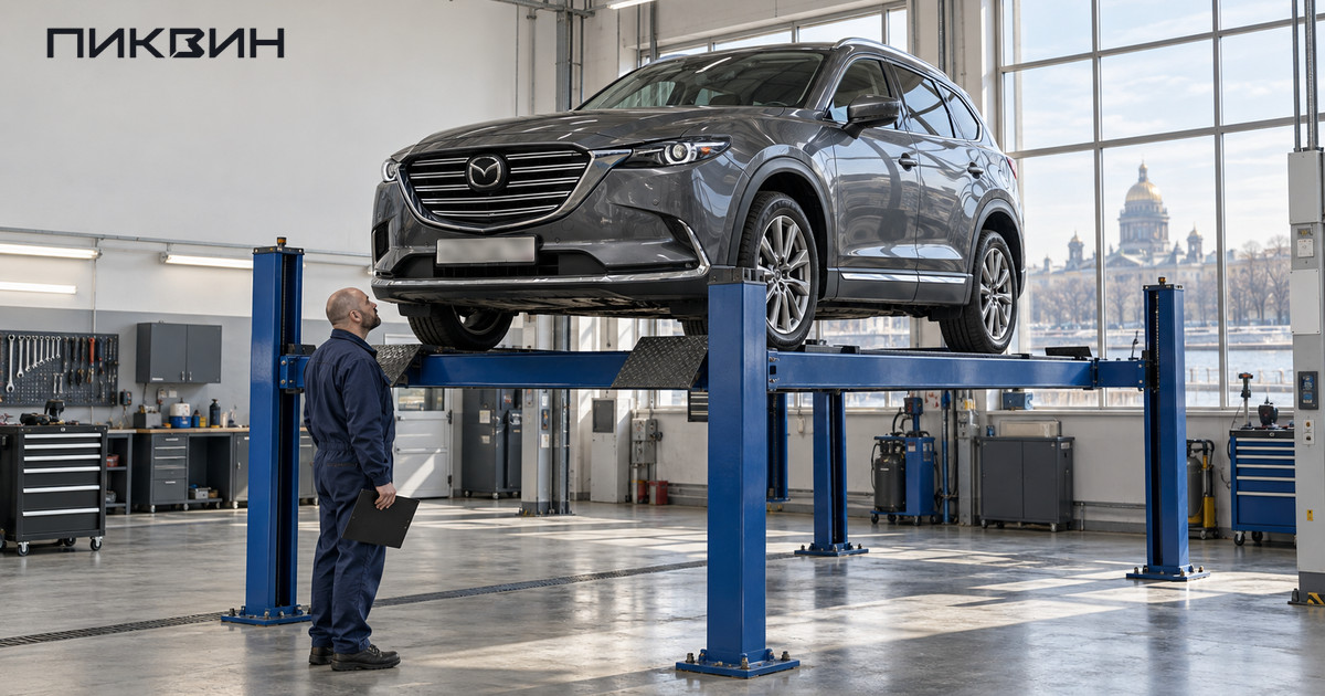 Mazda CX-9 на платформенном подъёмнике в сервисе; специалист осматривает автомобиль снизу.